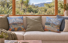 Load image into Gallery viewer, Two decorative throw pillows featuring a colorful landscape painting of mountains and trees, styled on a light beige sofa in a sunlit room with a large window showing a lush outdoor scene.