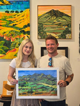 Load image into Gallery viewer, A customer holding an archival A2 giclee print of the Pirongia landscape painting by Miranda J Caird