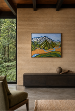 Load image into Gallery viewer, A framed landscape painting of green fields, a winding blue river, and snow-capped mountains, displayed on a textured beige wall in a modern interior setting.
