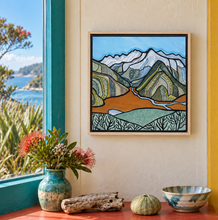 Load image into Gallery viewer, Routeburne Flats original painting in a natural wooden float frame hanging on a wall by a window. Pohutukawa blossoms are in a vase