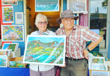Load image into Gallery viewer, Aroha fine art print by Miranda J Caird, customer holding print at Raglans tiny store . Colourful New Zealand landscape artwork